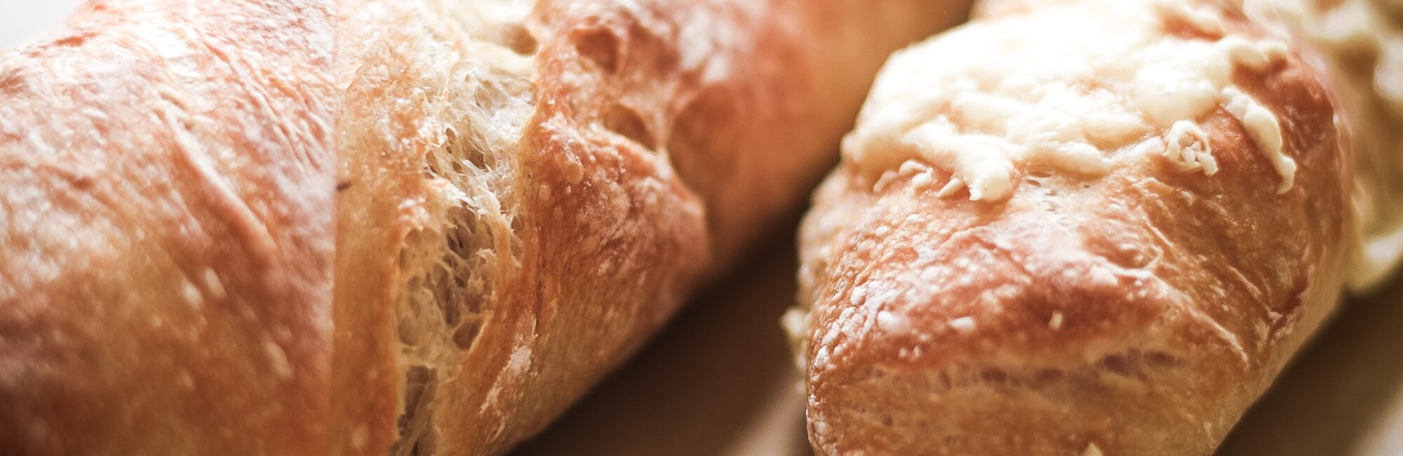 Zwei knusprige Wurzelbrote auf einem Bäckerleinen mit und ohne Käse überbacken