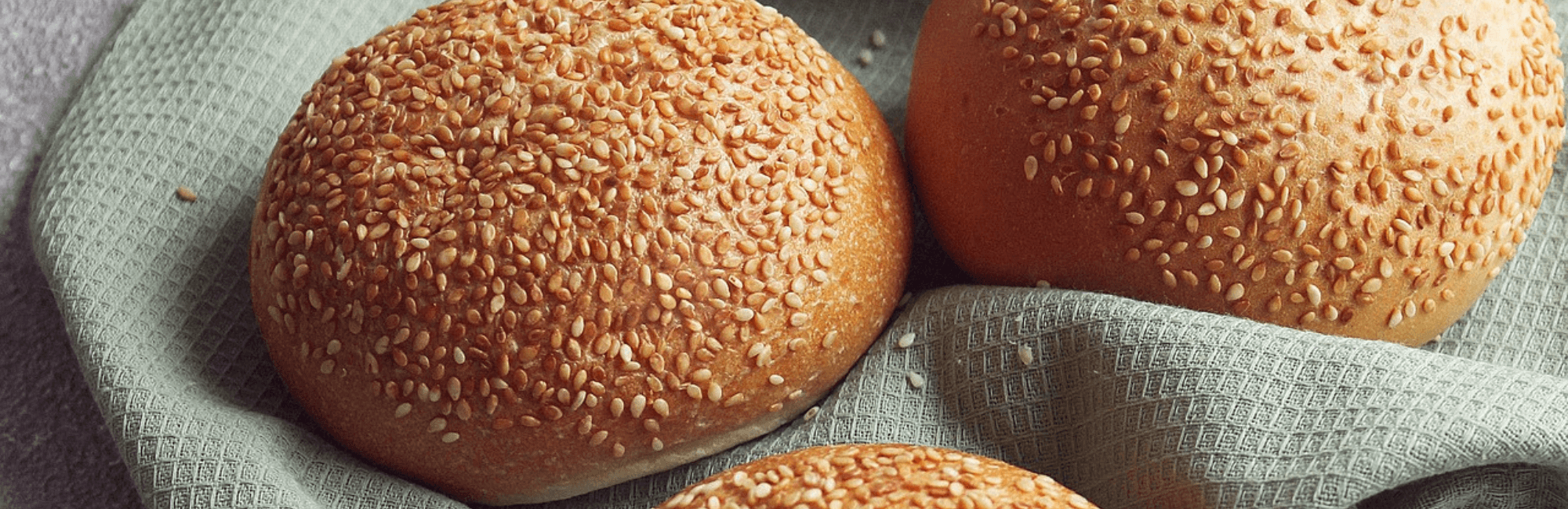 Burger Buns mit Sesam bestreut auf hellblauem Geschirrtuch