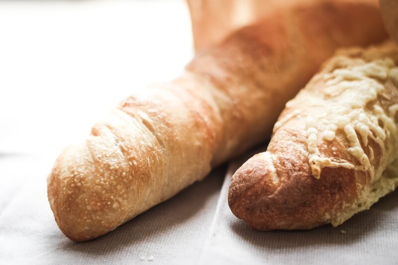 Zwei Wurzelbrote in einem Papiersäckchen, jeweils mit und ohne Käse überbacken